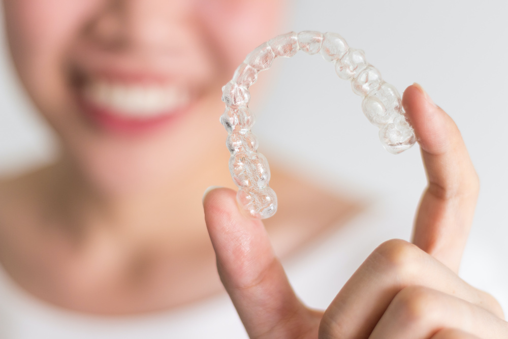 A smiling woman holding invisalign or invisible braces, orthodontic equipment