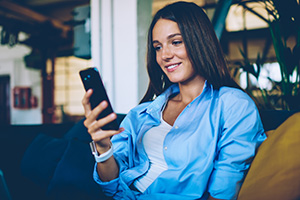 Positive caucasian female blogger enjoying of chatting online with followers from own popular web page, happy hipster girl holding smartphone gadget and downloading new application for communicate