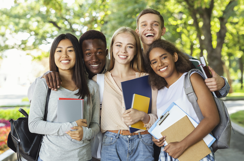 Group of international students having fun after studying Group of international happy students with books and notebooks having fun in park after studying, smiling at camera